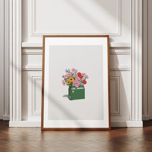 Op de afbeelding: Een ingelijste kunstdruk met een groene koeler gevuld met een kleurrijk boeket bloemen. De bloemen zijn roze, rood, geel en blauw. Het kunstwerk staat tegen een witte achtergrond en is ingelijst in een bruine houten lijst.