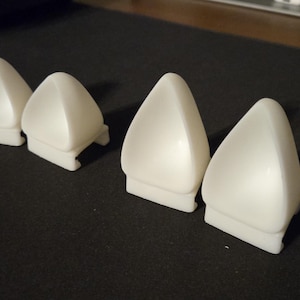 May include: Four white plastic triangular shaped objects with rounded edges. The objects are arranged in a row on a black surface.