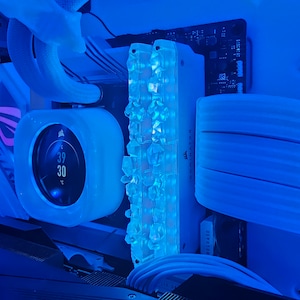 May include: Close-up of a computer's internal components, bathed in blue light. Features include a liquid cooler with a temperature display showing 39°C and 30°C, and a RAM module with illuminated crystal-like elements. The AORUS logo is visible.
