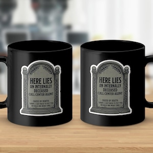 Könnte beinhalten: Zwei schwarze Keramikbecher mit einem humorvollen Grabsteindesign. Der Grabstein lautet "Here Lies An Internally Deceased Call Center Agent". Die Becher stehen auf einer Holzoberfläche.