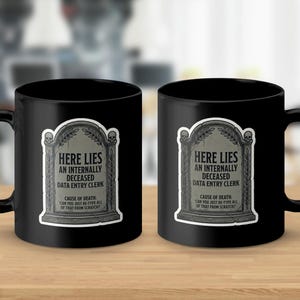 May include: Two black ceramic mugs with a humorous tombstone design. The tombstone reads "Here Lies An Internally Deceased Data Entry Clerk" with the text "Cause of Death: Can You Just Re-Type All of That From Scratch?"