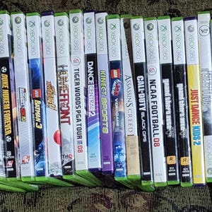 May include: A collection of 30 Xbox 360 video game cases, including titles such as Madden, Call of Duty, and Just Dance. The cases are arranged in a row, with the spines facing the viewer.
