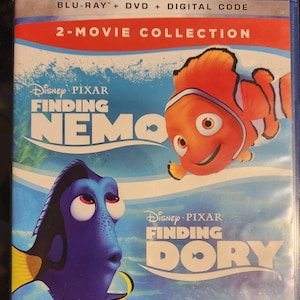 Puede incluir: Una caja de disco Blu-ray con las pel&iacute;culas de Disney Pixar Buscando a Nemo y Buscando a Dory. La caja tiene un fondo azul con im&aacute;genes de los personajes Nemo y Dory.