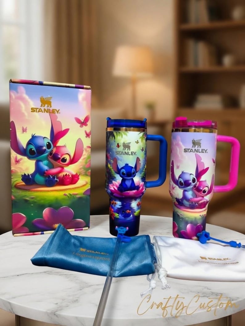 May include: A Stanley travel tumbler set featuring a colorful design of the characters Stitch and Angel. The set includes a tumbler with a blue handle, a tumbler with a pink handle, a box, a blue bag, and a white bag.