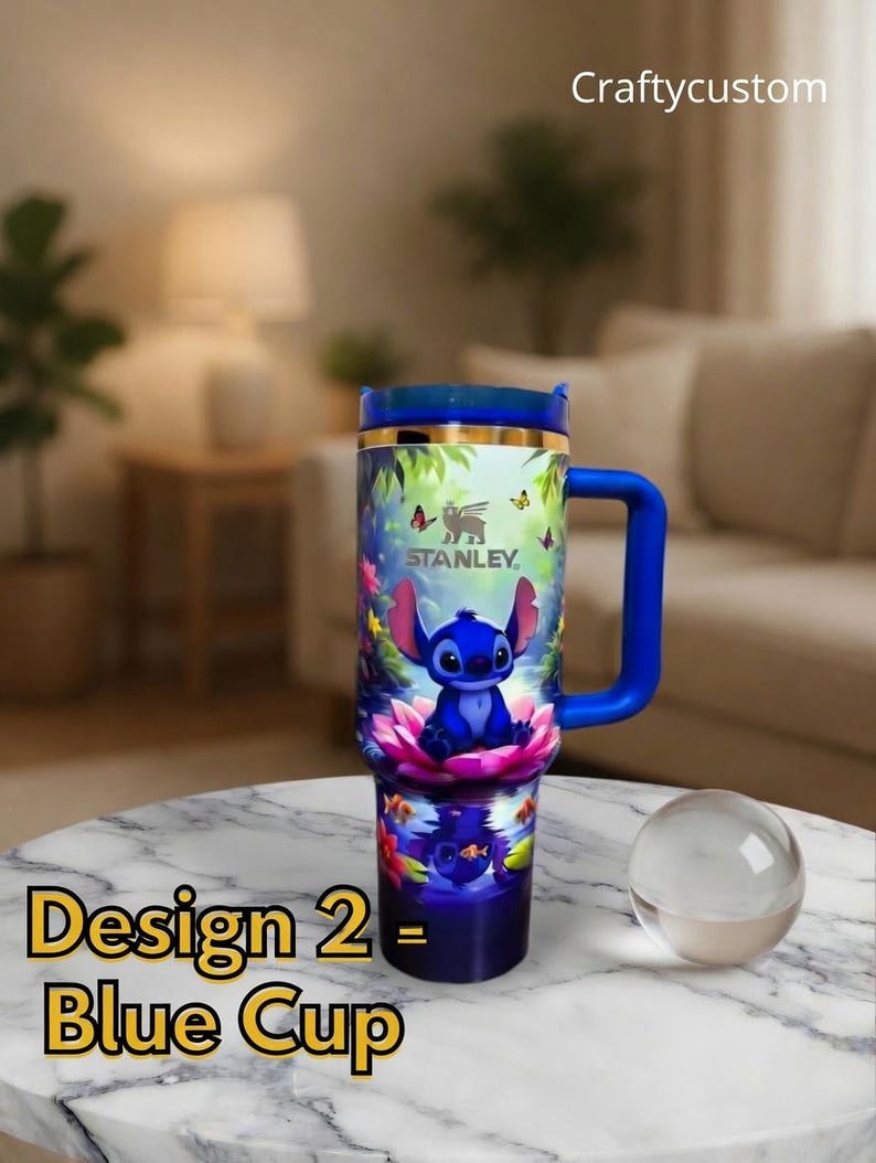 May include: Blue Stanley tumbler with a wraparound design featuring a cartoon character. The tumbler has a blue handle and lid, with the text "Craftycustom" at the top. The words "Design 2 - Blue Cup" are at the bottom.