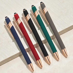 May include: Six colorful pens with gold-colored accents. The pens are arranged diagonally, showcasing a variety of colors including navy blue, red, black, green, and gray. Each pen has a sleek design with a stylus tip.