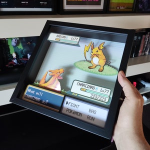 May include: A framed 3D pixel art scene of a Pokemon battle between Charizard and Raichu. The scene is set in a green grassy field with a blue sky. The text "What will CHARIZARD do?" is displayed on the screen. The options "FIGHT", "POKÉMON", "BAG", and "RUN" are also displayed on the screen.