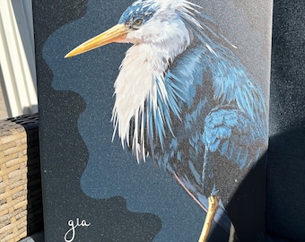 May include: A close-up of a painting of a blue heron with a white head and neck. The heron is perched on a branch with its head turned to the side. The background is a dark blue. The painting is signed "gia" in the bottom left corner.