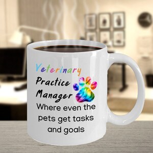 May include: White ceramic coffee mug with a black handle. The mug has a rainbow paw print and the text "Veterinary Practice Manager Where even the pets get tasks and goals".