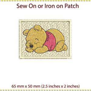 May include: Iron-on or sew-on patch featuring a cartoon Winnie the Pooh bear sleeping. The patch is beige with a white border and measures 6.5 cm by 5 cm.