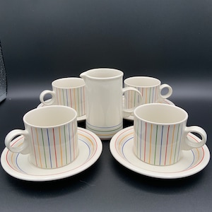 Puede incluir: Un juego de cinco tazas y platillos de cerámica blanca con patrones de rayas coloridas. El juego incluye una jarra de crema o un jarro de leche.