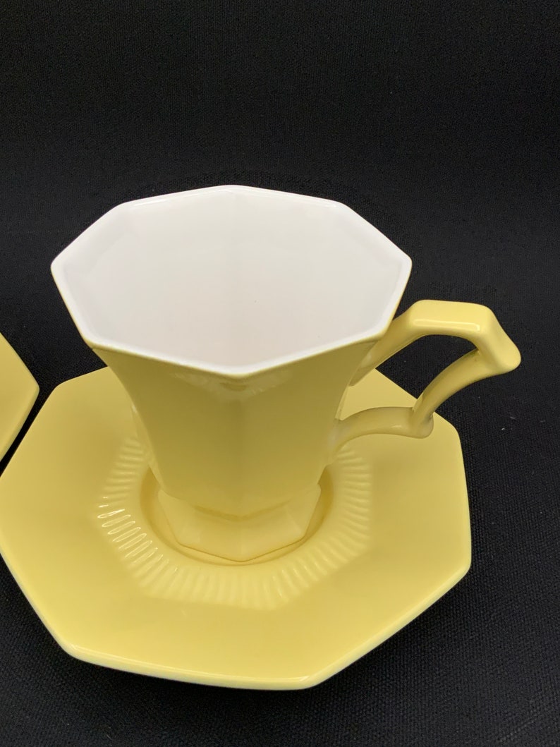 K&ouml;nnte beinhalten: Ein gelbes achteckiges Teetassen- und Untertassen-Set. Die Tasse hat ein wei&szlig;es Inneres und einen leicht ausgestellten Rand. Die Untertasse hat einen gewellten Rand.