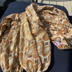 K&ouml;nnte beinhalten: Eine gemusterte Bluse in Gold- und Braunt&ouml;nen mit einem sich wiederholenden geometrischen Design aus Kreisen und Quadraten. Die langen &Auml;rmel sind an den Manschetten gerafft. Der Stoff ist ein leichtes Material in Gold-, Braun- und Cremet&ouml;nen.