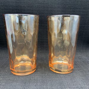 Puede incluir: Dos vasos vintage de color melocotón. Los vasos tienen un patrón texturizado, similar a un panal, en los lados y una base simple y redondeada. Los vasos están vacíos y se encuentran sobre una superficie oscura.