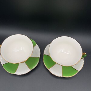 May include: Two white teacups with green and white striped saucers. The cups and saucers have a gold trim.