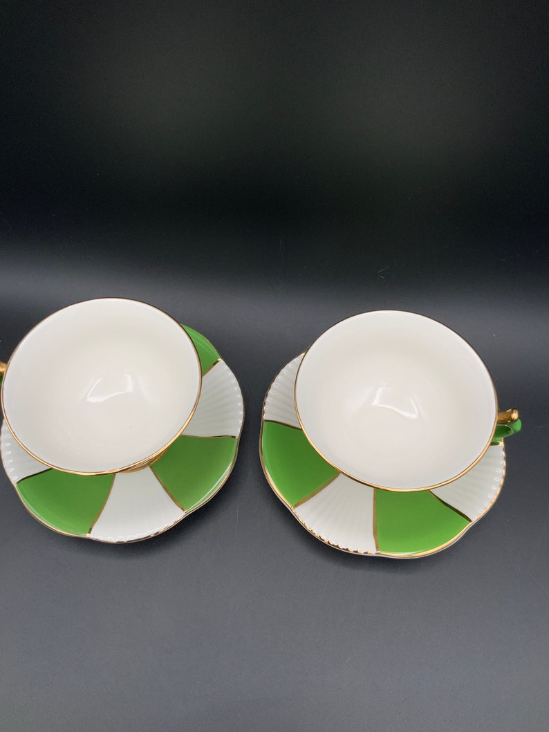 May include: Two white teacups with green and white striped saucers. The cups and saucers have a gold trim.