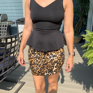 May include: A black sleeveless top with a V-neck and peplum waist paired with a leopard print mini skirt. The skirt features a brown and black animal print. The outfit is worn outdoors.