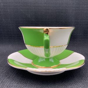 May include: A green and white teacup and saucer set with gold trim. The cup and saucer have a geometric pattern.