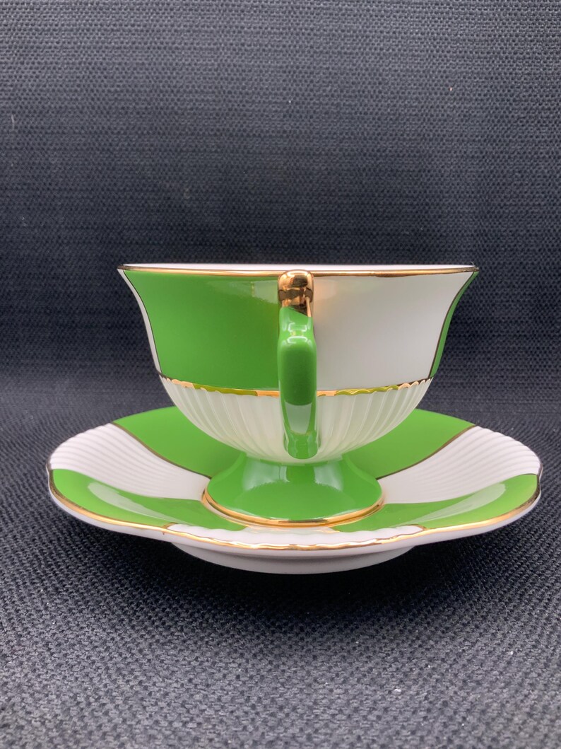 May include: A green and white teacup and saucer set with gold trim. The cup and saucer have a geometric pattern.