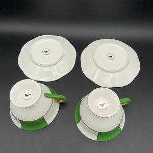 May include: Set of four white teacups and saucers with green and gold trim. The cups and saucers have a bird design on the bottom.