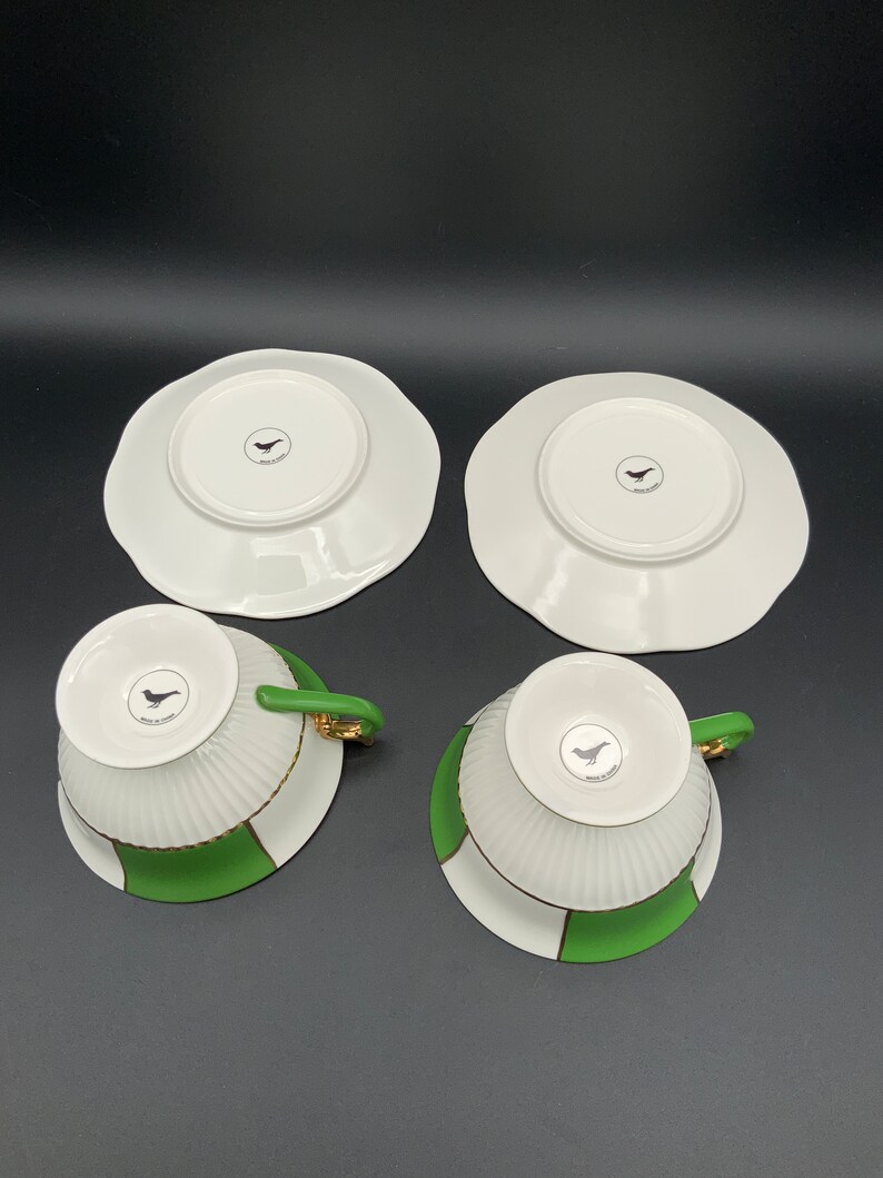May include: Set of four white teacups and saucers with green and gold trim. The cups and saucers have a bird design on the bottom.