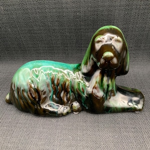 May include: A ceramic figurine of a dog lying down. The dog is brown and green with a glazed finish.