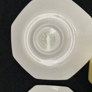 K&ouml;nnte beinhalten: Wei&szlig;e achteckige Untertasse mit einem gr&uuml;nen Logo in der Mitte. Das Logo ist ein stilisiertes Design mit dem Text "Made in England" im Inneren.