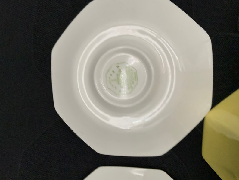 K&ouml;nnte beinhalten: Wei&szlig;e achteckige Untertasse mit einem gr&uuml;nen Logo in der Mitte. Das Logo ist ein stilisiertes Design mit dem Text "Made in England" im Inneren.