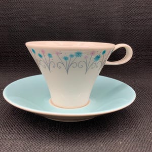 May include: A white teacup and saucer set with a blue and pink floral design. The saucer is a light blue colour.