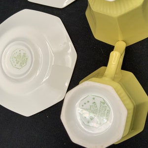 K&ouml;nnte beinhalten: Zwei gelbe achteckige Teetassen und Untertassen. Die Tassen haben ein wei&szlig;es Inneres mit einem gr&uuml;nen Blumendesign und den Text "Made in England" auf der Unterseite. Die Untertassen sind wei&szlig; mit einem gr&uuml;nen Blumendesign.