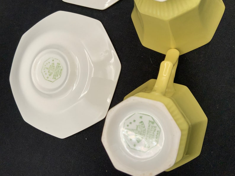 K&ouml;nnte beinhalten: Zwei gelbe achteckige Teetassen und Untertassen. Die Tassen haben ein wei&szlig;es Inneres mit einem gr&uuml;nen Blumendesign und den Text "Made in England" auf der Unterseite. Die Untertassen sind wei&szlig; mit einem gr&uuml;nen Blumendesign.