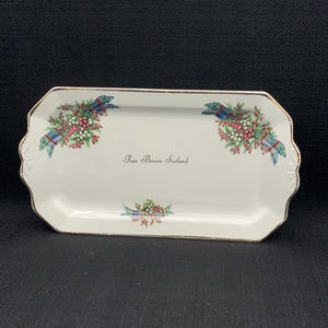 May include: A white rectangular serving tray with a gold rim and a floral design. The tray features a tartan ribbon with the text "From Bonnie Scotland".