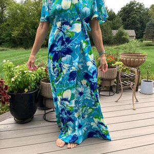 Puede incluir: Un vestido cruzado largo hasta los pies con un estampado floral vibrante en tonos azul brillante, azul marino, blanco y verde lima. El vestido tiene mangas cortas con vuelo, escote en V y un lazo lateral que asegura los paneles frontales.