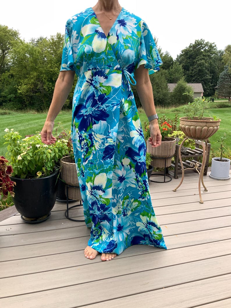Puede incluir: Un vestido cruzado largo hasta los pies con un estampado floral vibrante en tonos azul brillante, azul marino, blanco y verde lima. El vestido tiene mangas cortas con vuelo, escote en V y un lazo lateral que asegura los paneles frontales.