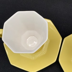 K&ouml;nnte beinhalten: Ein gelber achteckiger Unterteller mit einer wei&szlig;en achteckigen Teetasse darauf. Der Unterteller hat ein dekoratives Muster am Rand.