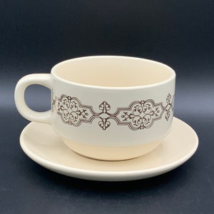 May include: A white ceramic teacup and saucer set with a brown decorative pattern. The cup has a wide rim and a handle.
