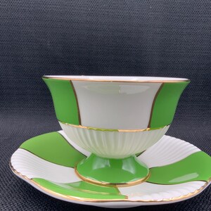May include: A white and green teacup and saucer set with a gold trim. The cup and saucer have a chequered pattern.