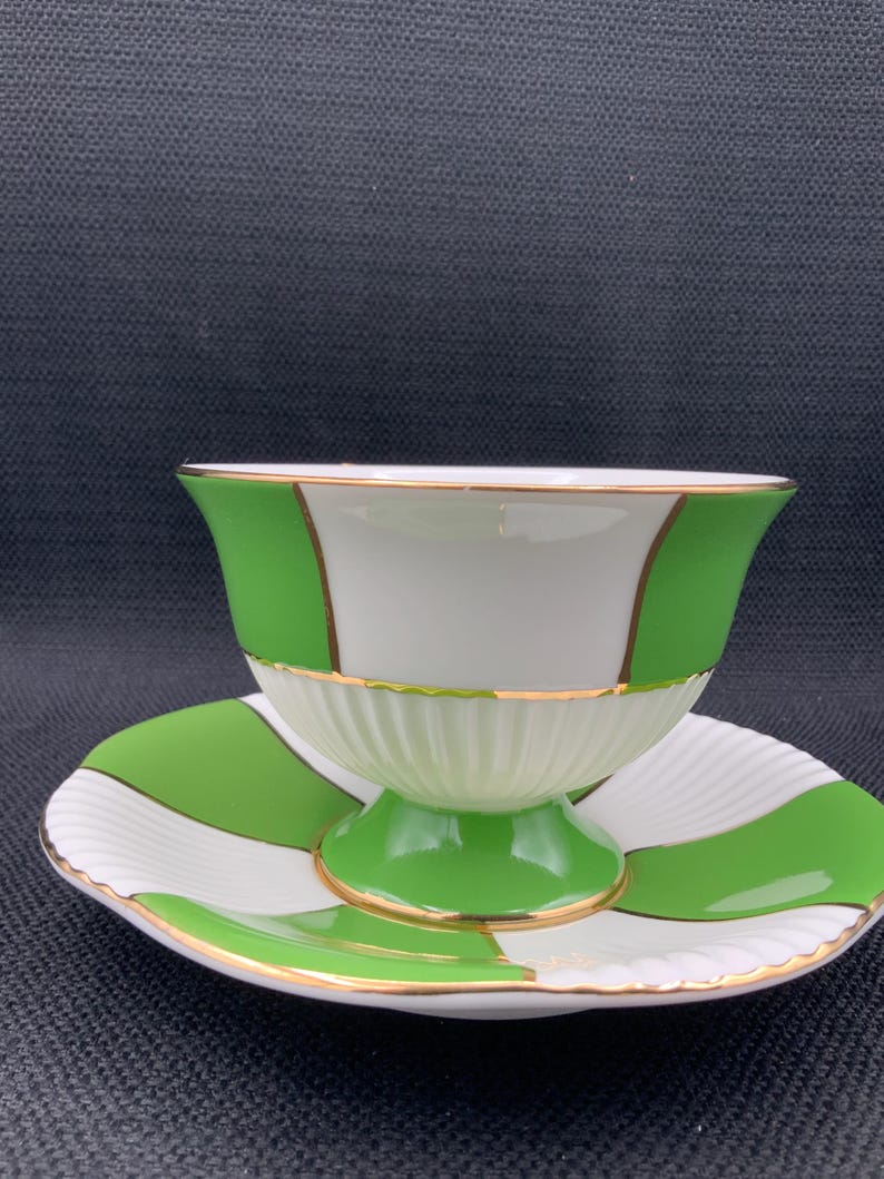 May include: A white and green teacup and saucer set with a gold trim. The cup and saucer have a chequered pattern.