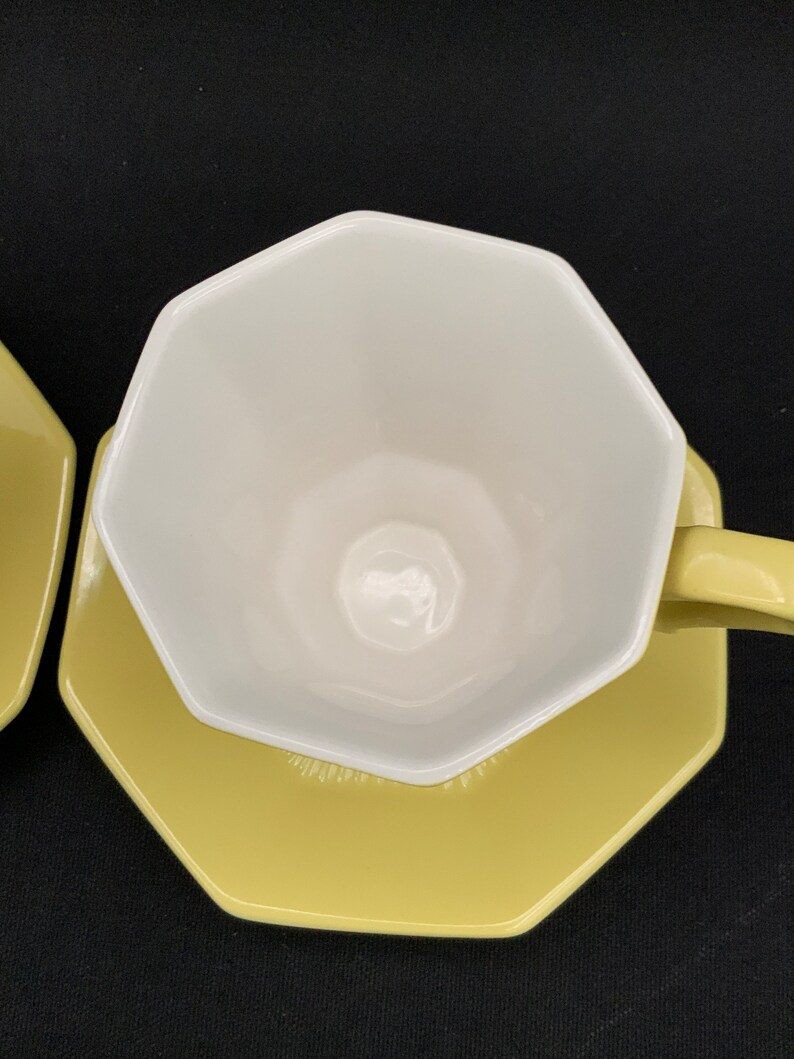 K&ouml;nnte beinhalten: Eine gelbe achteckige Untertasse mit einer wei&szlig;en achteckigen Teetasse darauf. Tasse und Untertasse sind beide aus Keramik.