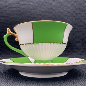 May include: A white and green teacup and saucer set with gold trim. The cup and saucer have a geometric pattern with white, green, and gold accents.
