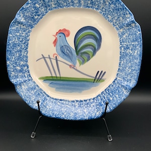 Puede incluir: Un plato de cerámica azul y blanco con un diseño de gallo. El plato tiene un borde festoneado y un esmalte azul moteado.