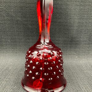 May include: A red glass bell with a textured surface and a clear glass handle. The bell is decorated with small, raised dots.