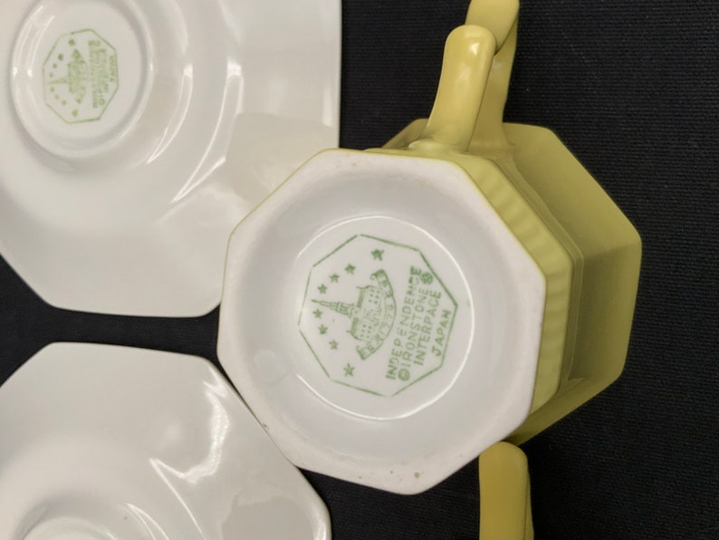 K&ouml;nnte beinhalten: Ein Set aus vier gelben Teetassen und Untertassen. Die Tassen und Untertassen haben eine achteckige Form. Auf der Unterseite der Tassen und Untertassen befindet sich ein gr&uuml;nes Logo mit der Aufschrift "INDEPENDENT IRONSTONE INTERSPACE JAPAN".