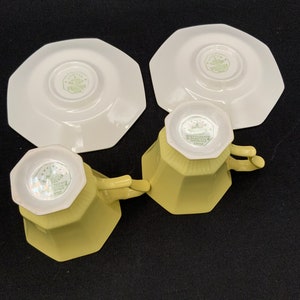 K&ouml;nnte beinhalten: Zwei gelbe Teetassen und Untertassen mit einem wei&szlig;en achteckigen Design. Die Tassen und Untertassen haben ein gr&uuml;nes Blumenmuster auf der Unterseite.