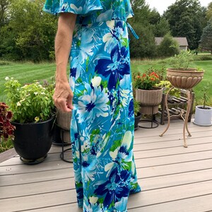 Puede incluir: Un vestido largo hasta los pies con un estampado floral vibrante en tonos azul brillante, azul marino y verde lima. La prenda tiene mangas cortas y fluidas, un escote en V y un detalle de cord&oacute;n ajustable en la cintura en el lateral.