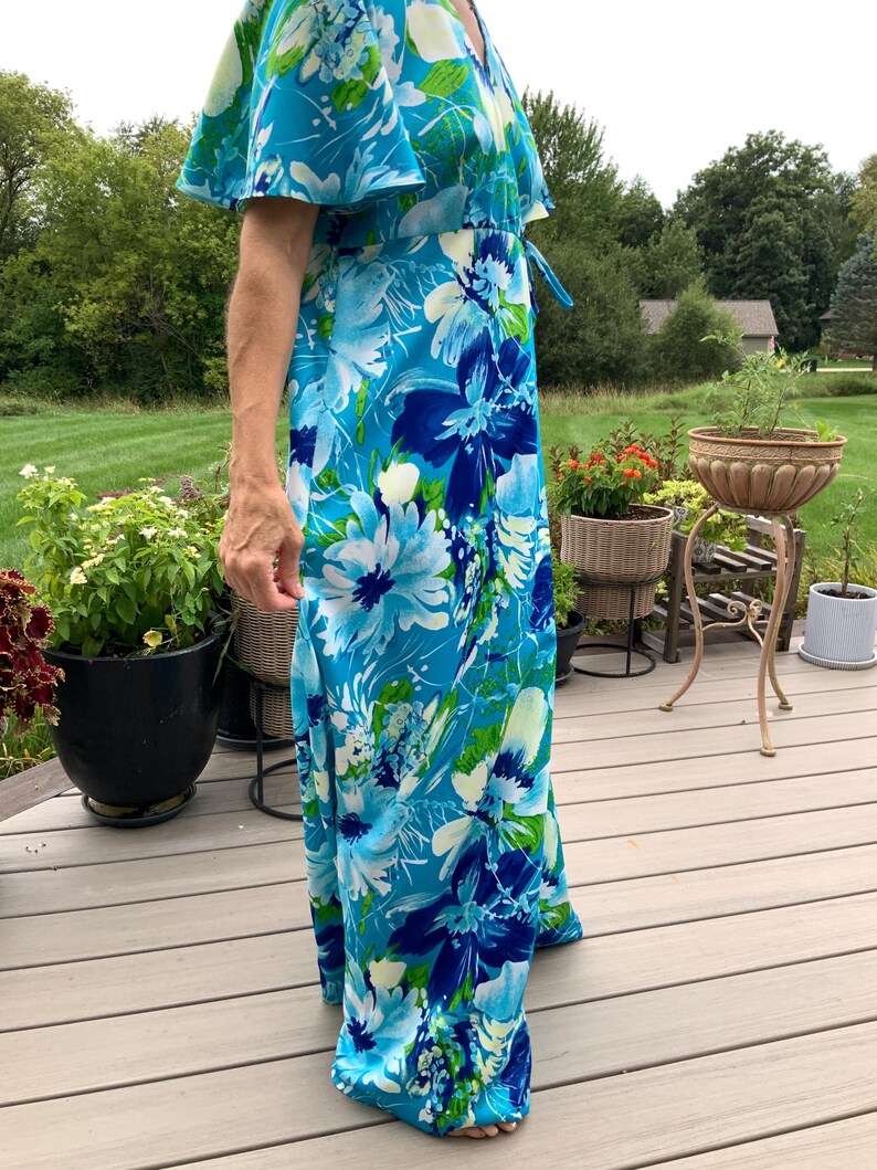 Puede incluir: Un vestido largo hasta los pies con un estampado floral vibrante en tonos azul brillante, azul marino y verde lima. La prenda tiene mangas cortas y fluidas, un escote en V y un detalle de cord&oacute;n ajustable en la cintura en el lateral.