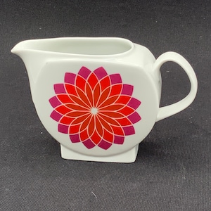 Puede incluir: Crema de cerámica blanca con un diseño de flor geométrico en tonos rojos, rosas y naranjas.