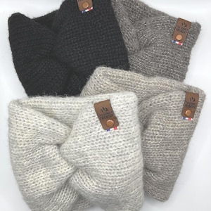 Puede incluir: Cuatro diademas de punto en tonos negro, gris y blanco roto. Cada diadema presenta un diseño de nudo retorcido y una pequeña etiqueta de cuero marrón con el texto "THE BONNET FRENCHY". Las etiquetas también tienen una pequeña bandera francesa.