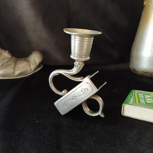 May include: A silver candlestick with a decorative design and a match holder attached to the base.
