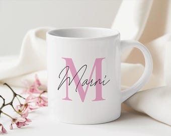 Könnte beinhalten: Weiße Keramiktasse mit einem rosa Buchstaben "M" und dem Namen "Marni" in schwarzer Schrift.